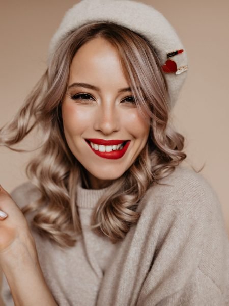Lovely french girl playing with her curls on brown background. Blithesome white lady in beret laughing in studio
